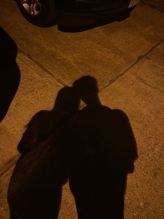 the shadow of a person standing next to a parked car on a sidewalk at night