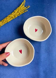 two white bowls with hearts painted on them, one being held up by a hand