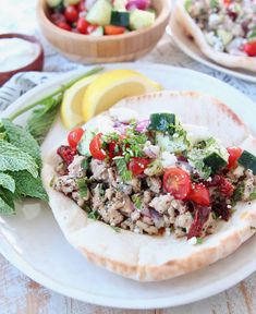 a pita filled with meat and vegetables on top of a white plate next to lemon wedges