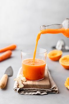 an orange juice being poured into a glass on top of a cutting board next to sliced carrots