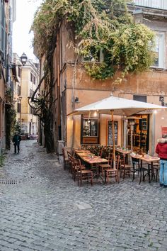 people are sitting at tables in an alleyway with tall buildings on either side and one person walking by