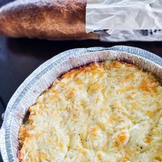 a close up of a pie in a pan on a table with bread behind it