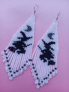 two black and white beaded earrings on a pink background, one is shaped like a cat