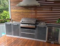 an outdoor kitchen with grill, sink and cabinets on the outside deck overlooking trees in the background