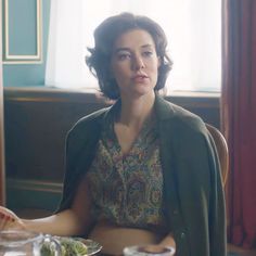 a woman sitting at a table in front of a plate of food and looking off into the distance