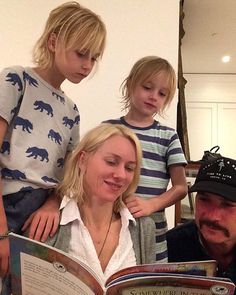 a man and two children are looking at a book with an adult in the background