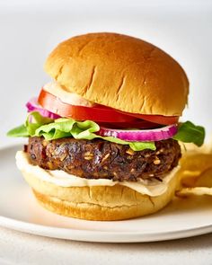 a hamburger with lettuce, tomato and onion on a plate next to chips