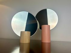 two round mirrors sitting next to each other on top of a wooden table in front of a white wall