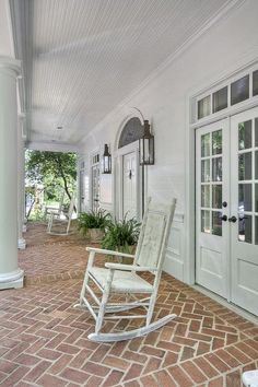 a rocking chair on the front porch of a house with white doors and brick flooring