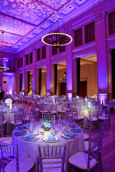 a banquet hall with tables and chairs set up for an event or function, lit by purple lighting