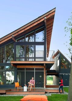 two people are sitting on chairs in front of a house with large windows and an orange pillow