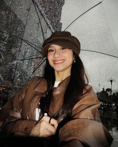 a woman standing in the rain with an umbrella over her head and smiling at the camera