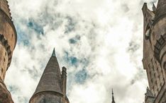 looking up at the spires and towers of an old castle like building on a cloudy day