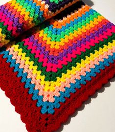 a multicolored crocheted blanket laying on top of a white table next to two pillows