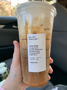 a person holding up a plastic cup filled with iced coffee in the back seat of a car