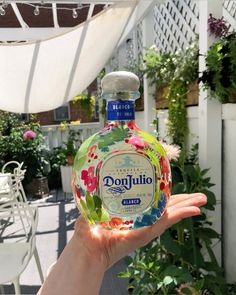 a hand holding a bottle of donjuto in front of a patio with potted plants