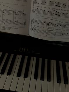 an open book with sheet music and piano keys on it's cover, in front of a piano keyboard