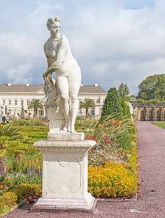 there is a white statue in the middle of a garden with many flowers and trees