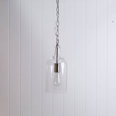 a clear glass light hanging from a chain on a white wall with wood paneling