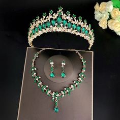 a green and white tiara with matching necklace and earrings on a black surface next to flowers