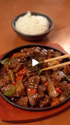 beef and vegetable stir fry with chopsticks in a pan on a table next to rice