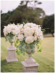 two vases filled with white flowers sitting on top of cement pillars in the grass