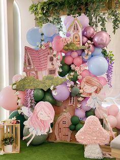 a table topped with lots of balloons next to a green carpeted floor covered in greenery