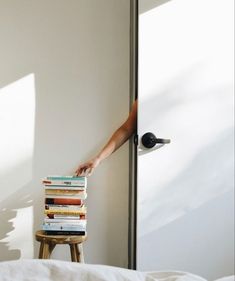 a stack of books sitting on top of a wooden stool next to a white wall