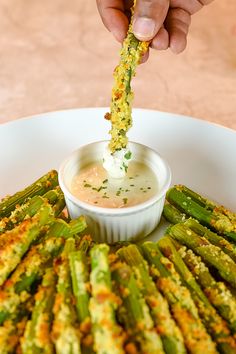 a person dipping sauce on asparagus in a white bowl with other food items