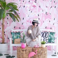 a woman sitting on a bench in front of a wall with flamingos and palm trees