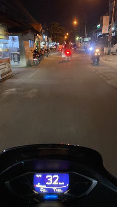 a motorcycle driving down a street at night with lights on and people riding motorcycles in the background