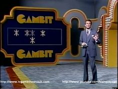 a man standing in front of a sign on a tv set with his hands up