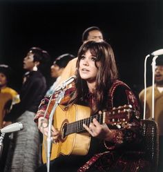 a woman sitting in front of a microphone while holding a guitar