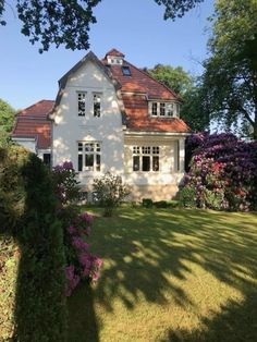 a large white house with red roof and flowers in the foreground, on a sunny day