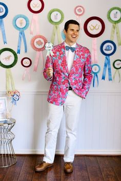 a man in a pink jacket and bow tie holding up a paper plate with ribbons on it