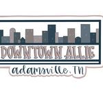 the downtown allig logo is shown in brown and white, with city buildings behind it