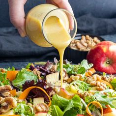 someone pouring dressing onto a salad with apples and walnuts