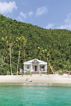 a small white house sitting on top of a sandy beach next to the ocean with palm trees