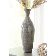 a vase with dried grass in it on a table next to a ball and window