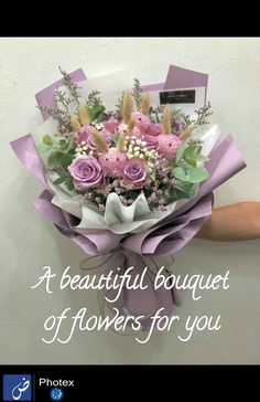 a bouquet of purple flowers is held up against a white wall by someone's hand