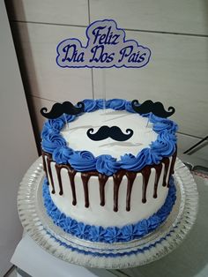 a cake decorated with blue icing and chocolate drips on a white plate in front of a sign that reads feliz dia de des puis