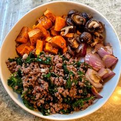 a white bowl filled with meat, vegetables and other foods on top of a table