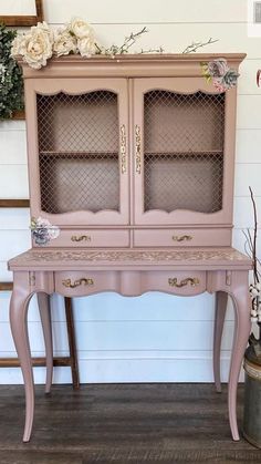 an antique pink desk with glass doors and flowers on top