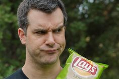 a man holding a bag of lays chips in his left hand and looking at the camera