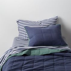 a bed with blue and green pillows on top of it, next to a white wall