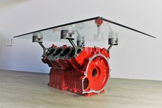 a red engine sitting on top of a wooden floor next to a glass table with wheels