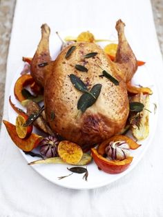 a roasted turkey on a white plate with oranges and herbs