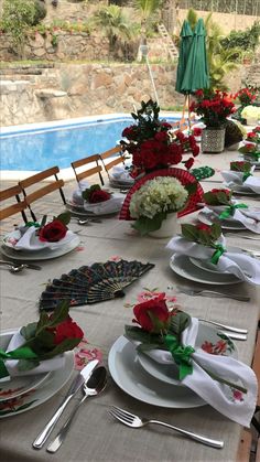 the table is set with white plates and silverware, red flowers, and green napkins