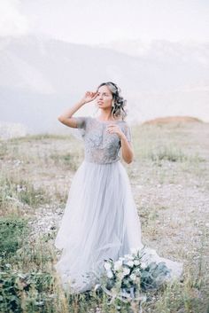 a woman in a white dress standing on top of a grass covered field next to mountains