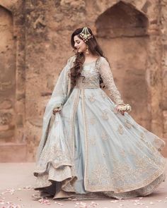 a woman in a white and blue wedding gown standing on the ground with her hands behind her back